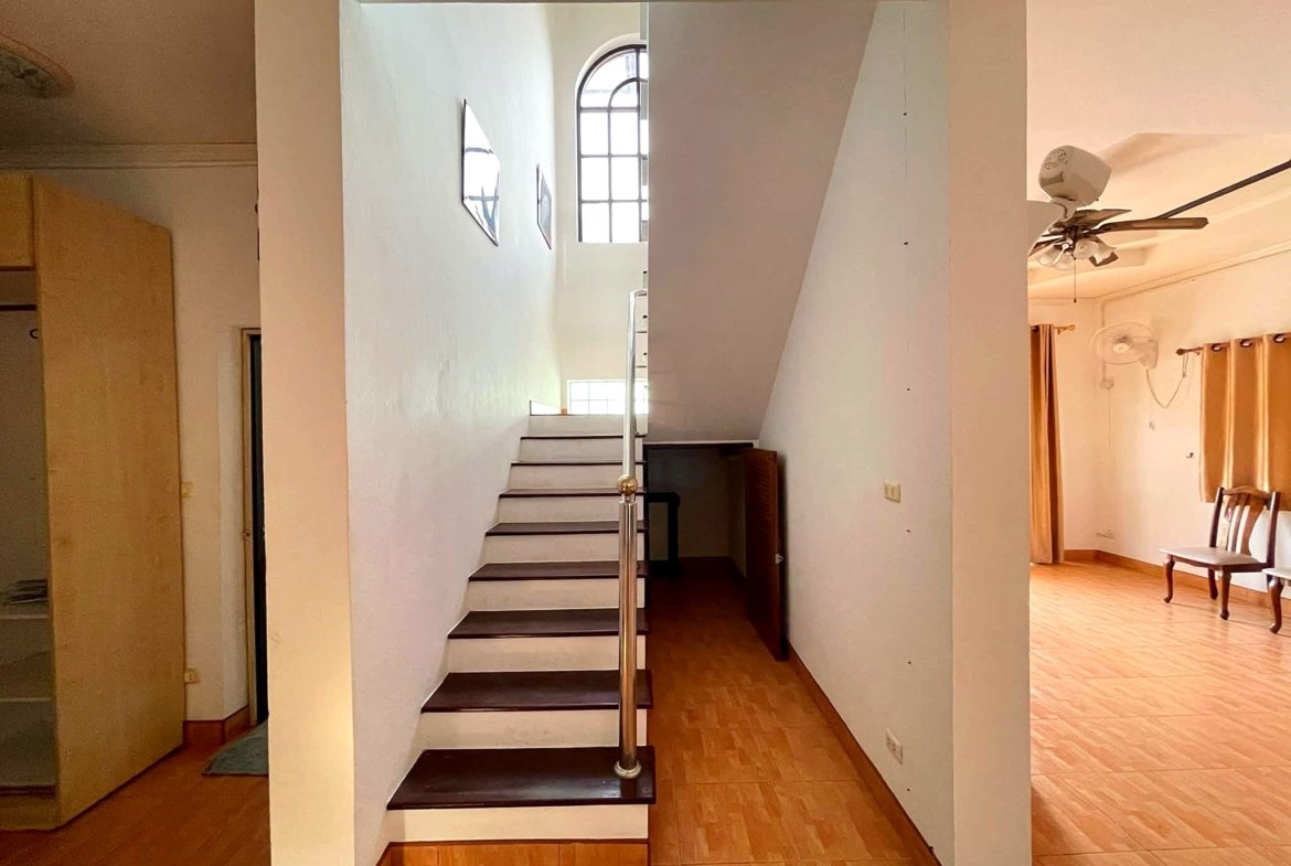 Bright interior featuring a straight staircase along a white wall with a curved arched window at the top and a metal handrail along the steps.