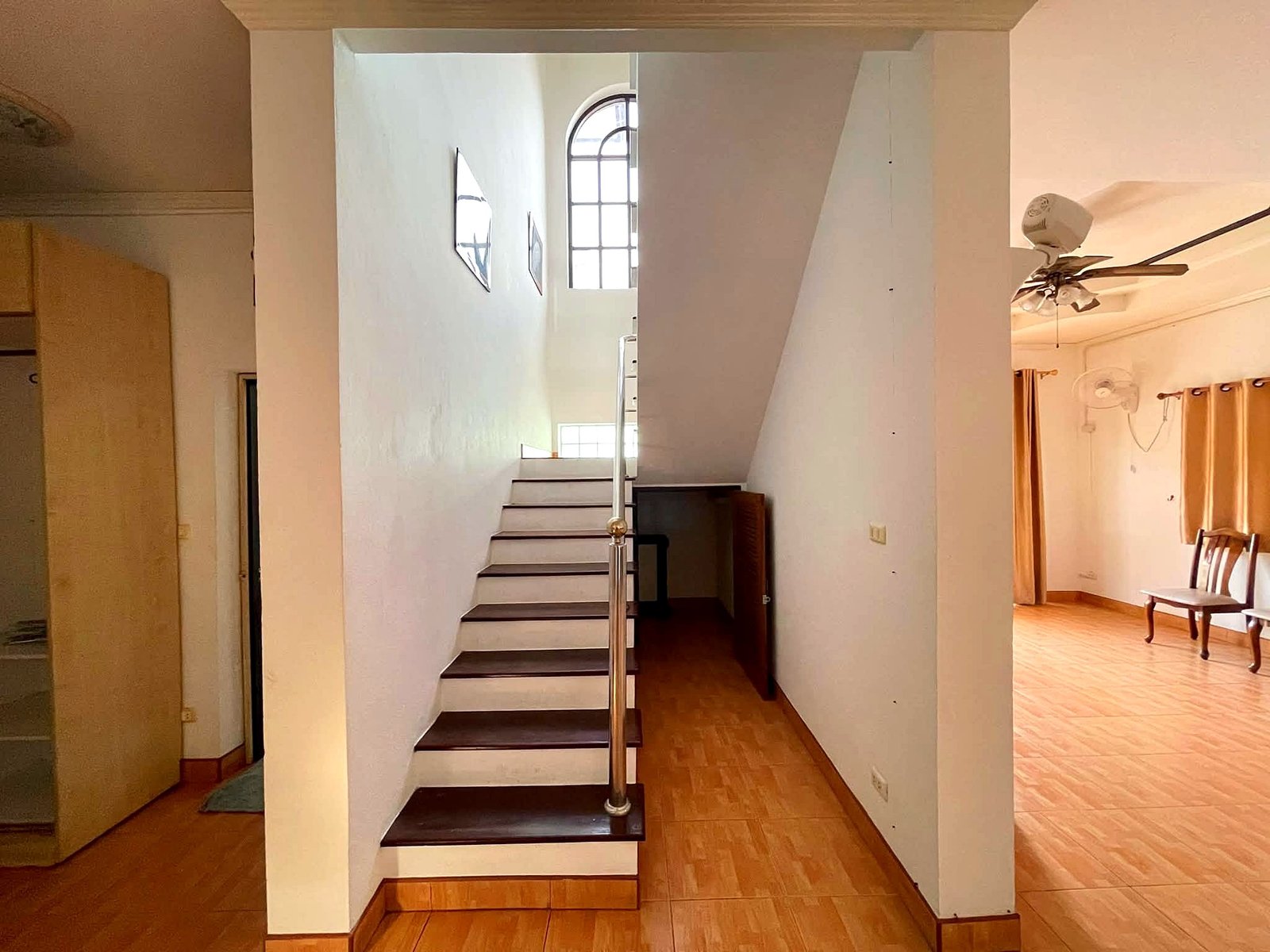 Poolvilla_Pattaya_Rent_Rdl352_8 Bright interior featuring a straight staircase along a white wall with a curved arched window at the top and a metal handrail along the steps.