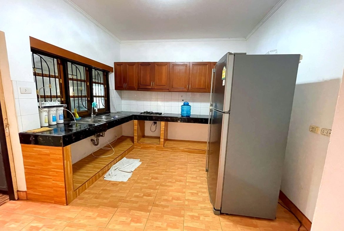 Kitchen with brown wooden cabinets, black countertops, a stainless steel refrigerator, sink, and gas stove; tiled floor and barred window on the left.