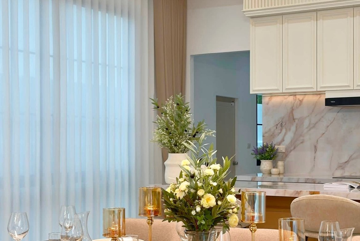 Elegant dining table set with white dishes, gold cutlery and candleholders, and a floral centerpiece.
