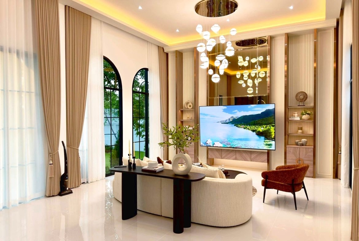 Elegant living room with beige floor-to-ceiling curtains, arched windows, and a large flat-screen TV.