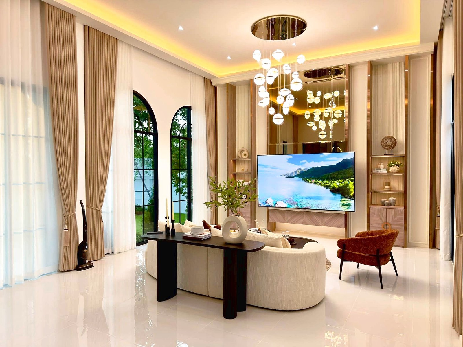 Poolvilla_Soi_Siam_Pattaya_Dlh584_13 Elegant living room with beige floor-to-ceiling curtains, arched windows, and a large flat-screen TV.