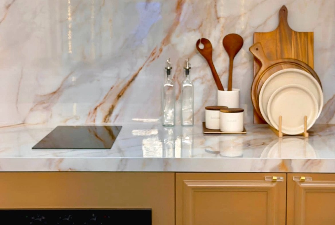 Open cookbook on a marble kitchen counter with plates, cutting boards, and wooden utensils nearby.