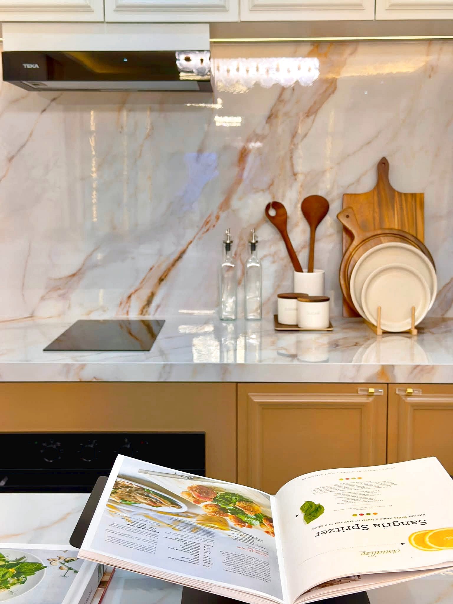 Poolvilla_Soi_Siam_Pattaya_Dlh584_18 Open cookbook on a marble kitchen counter with plates, cutting boards, and wooden utensils nearby.