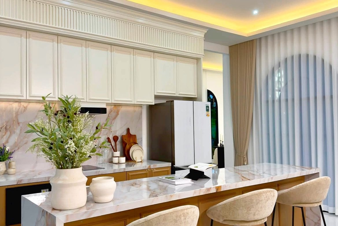 Modern kitchen with marble island, white cabinets, and beige upholstered bar stools along a marble countertop.