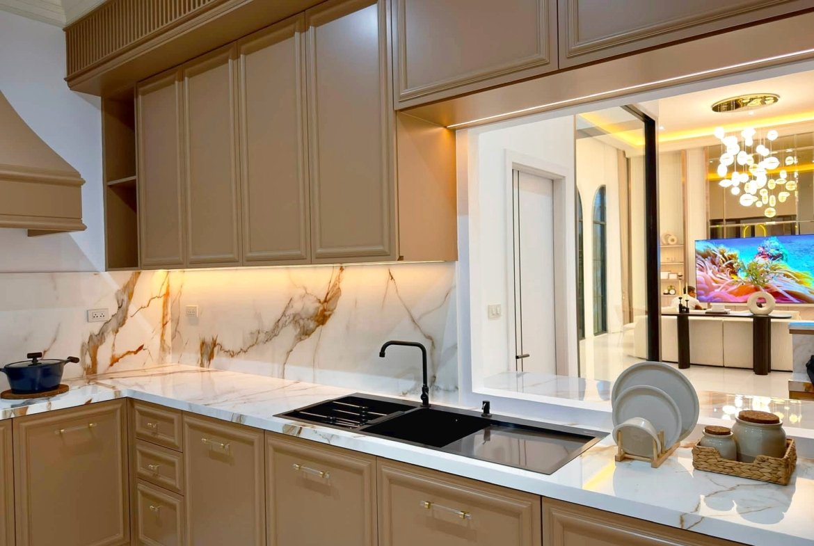 Modern kitchen with beige cabinetry, marble countertops, and a black sink and stovetop forming an L-shape island.