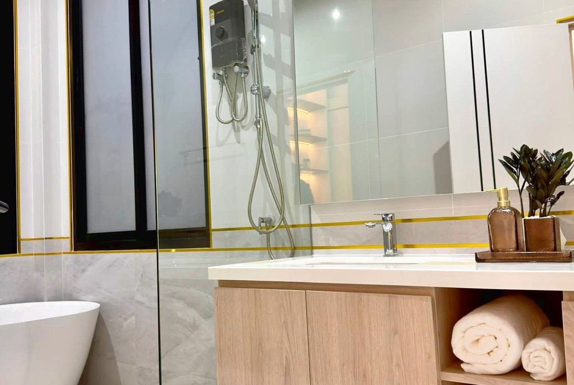 Modern bathroom featuring a glass-walled shower, a freestanding tub, and a light wood vanity with open shelves holding rolled towels and a small plant.