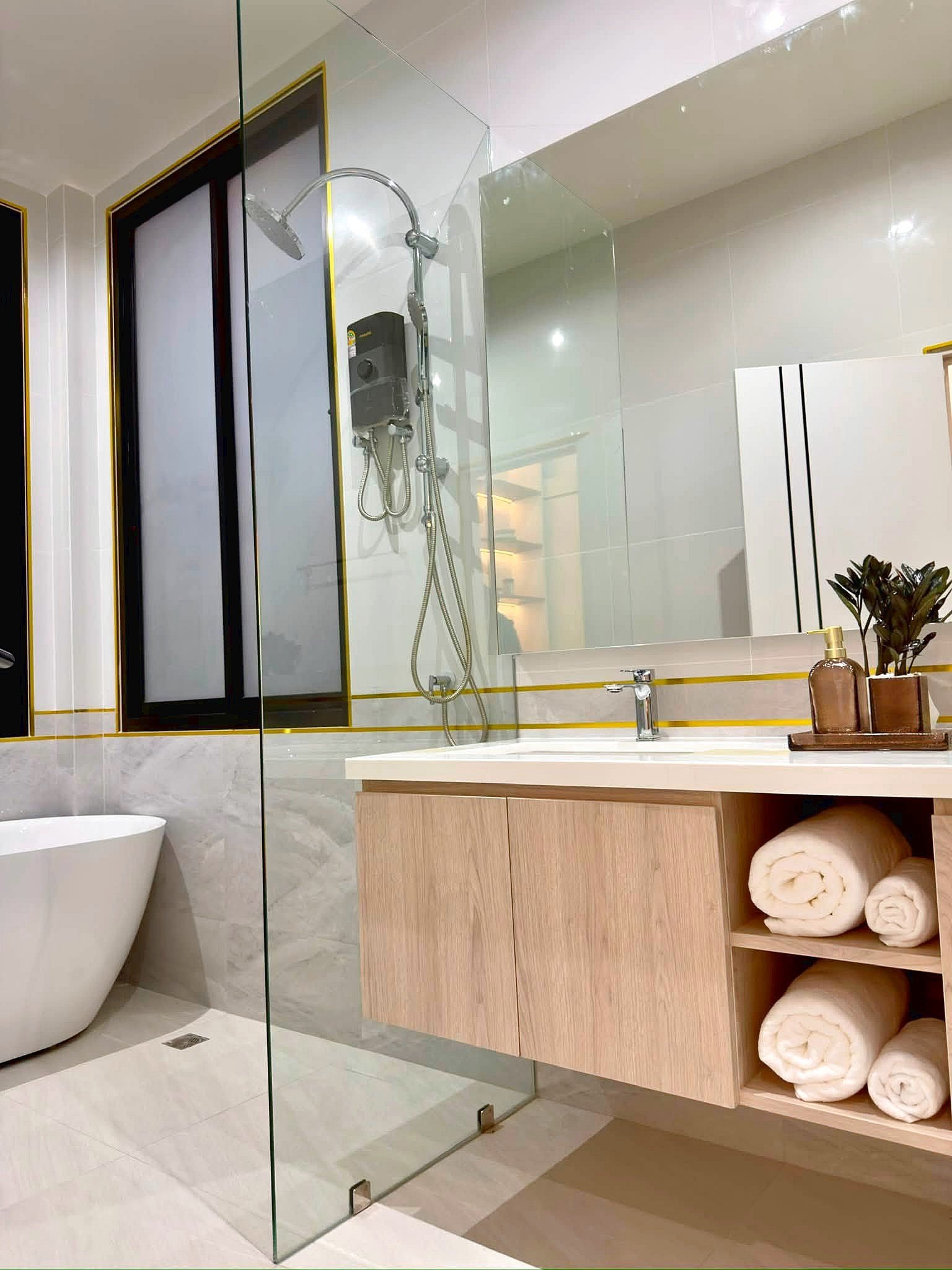 Poolvilla_Soi_Siam_Pattaya_Dlh584_27 Modern bathroom featuring a glass-walled shower, a freestanding tub, and a light wood vanity with open shelves holding rolled towels and a small plant.