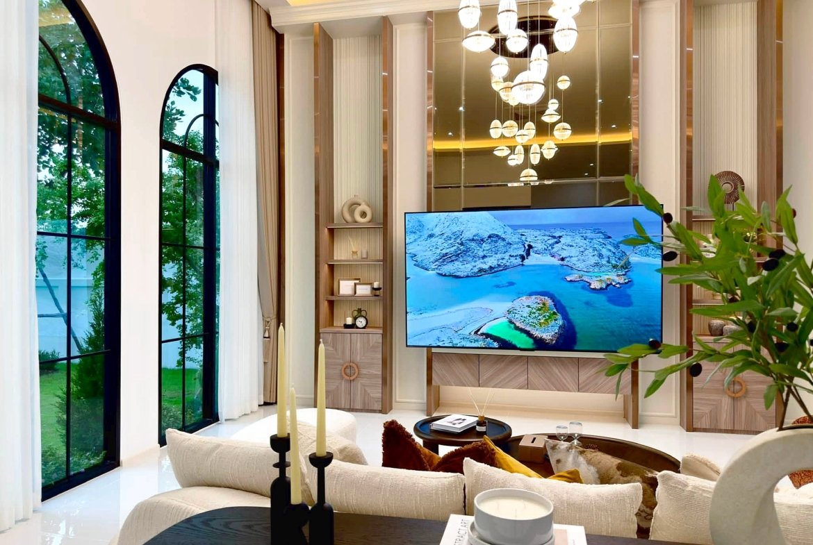 Luxurious living room with arched windows, cream sofas, and a large TV displaying a snowy coastline.