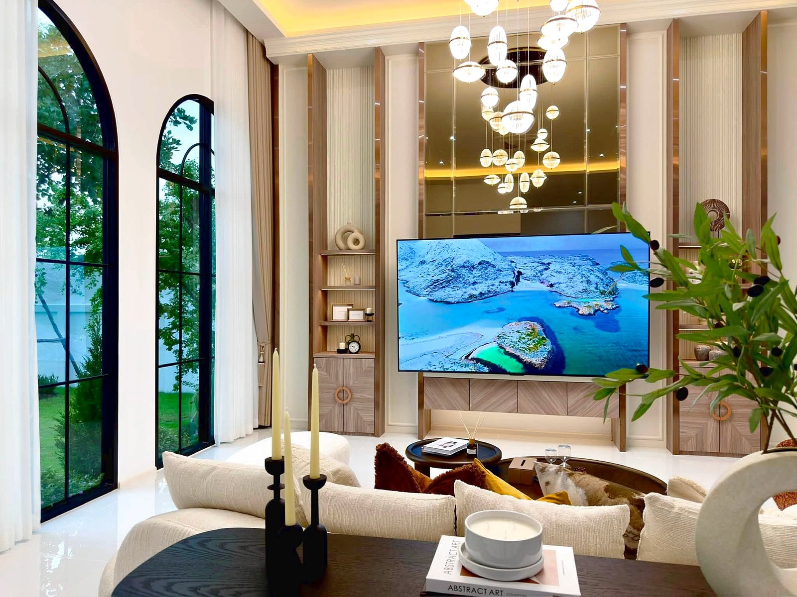 Poolvilla_Soi_Siam_Pattaya_Dlh584_3 Luxurious living room with arched windows, cream sofas, and a large TV displaying a snowy coastline.