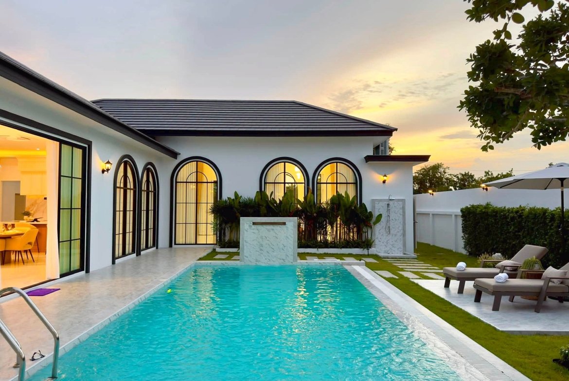 Modern white villa with arched black-framed windows, poolside patio, and sunset lighting.