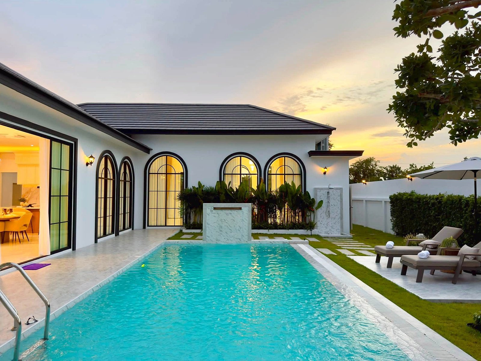 Poolvilla_Soi_Siam_Pattaya_Dlh584_31 Modern white villa with arched black-framed windows, poolside patio, and sunset lighting.