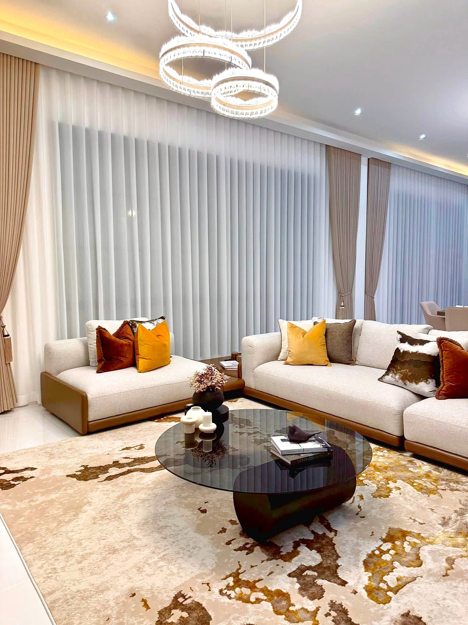 Poolvilla_Soi_Siam_Pattaya_Dlh584_4 Modern living room with a cream sectional, orange pillows, and a round glass coffee table on a gold-toned rug under soft lighting.