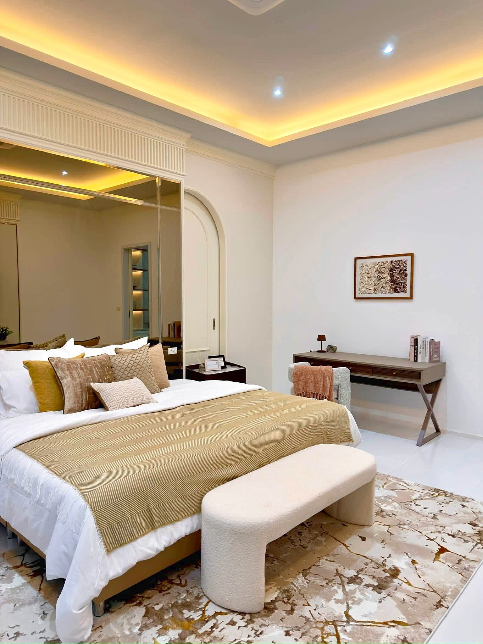 Poolvilla_Soi_Siam_Pattaya_Dlh584_5 Hotel-style bedroom with beige-gold bed linens and multiple throw pillows, a white bench at the foot, and a patterned rug.