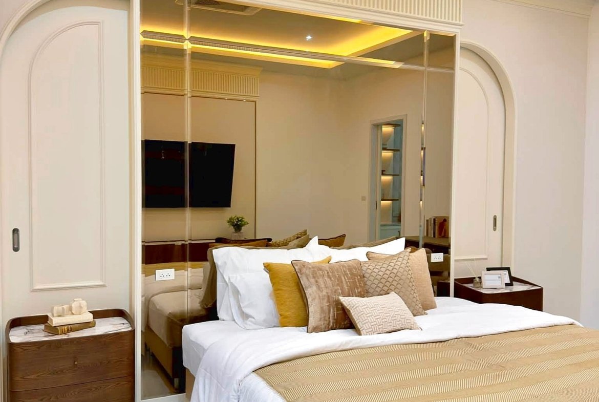 Luxurious bedroom with a large bed, beige and gold accents, mirrored headboard and warm cove lighting.