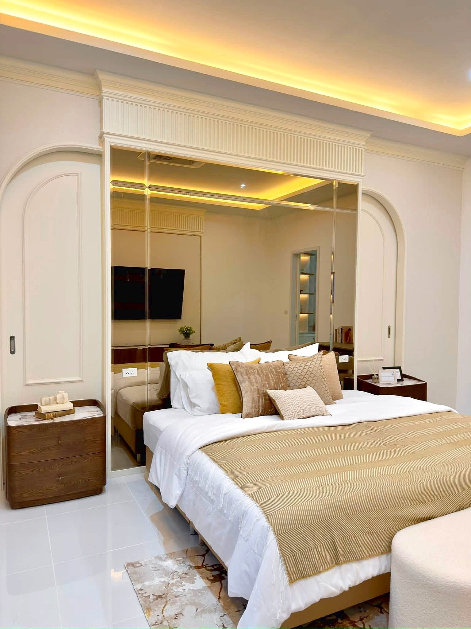 Poolvilla_Soi_Siam_Pattaya_Dlh584_7 Luxurious bedroom with a large bed, beige and gold accents, mirrored headboard and warm cove lighting.",