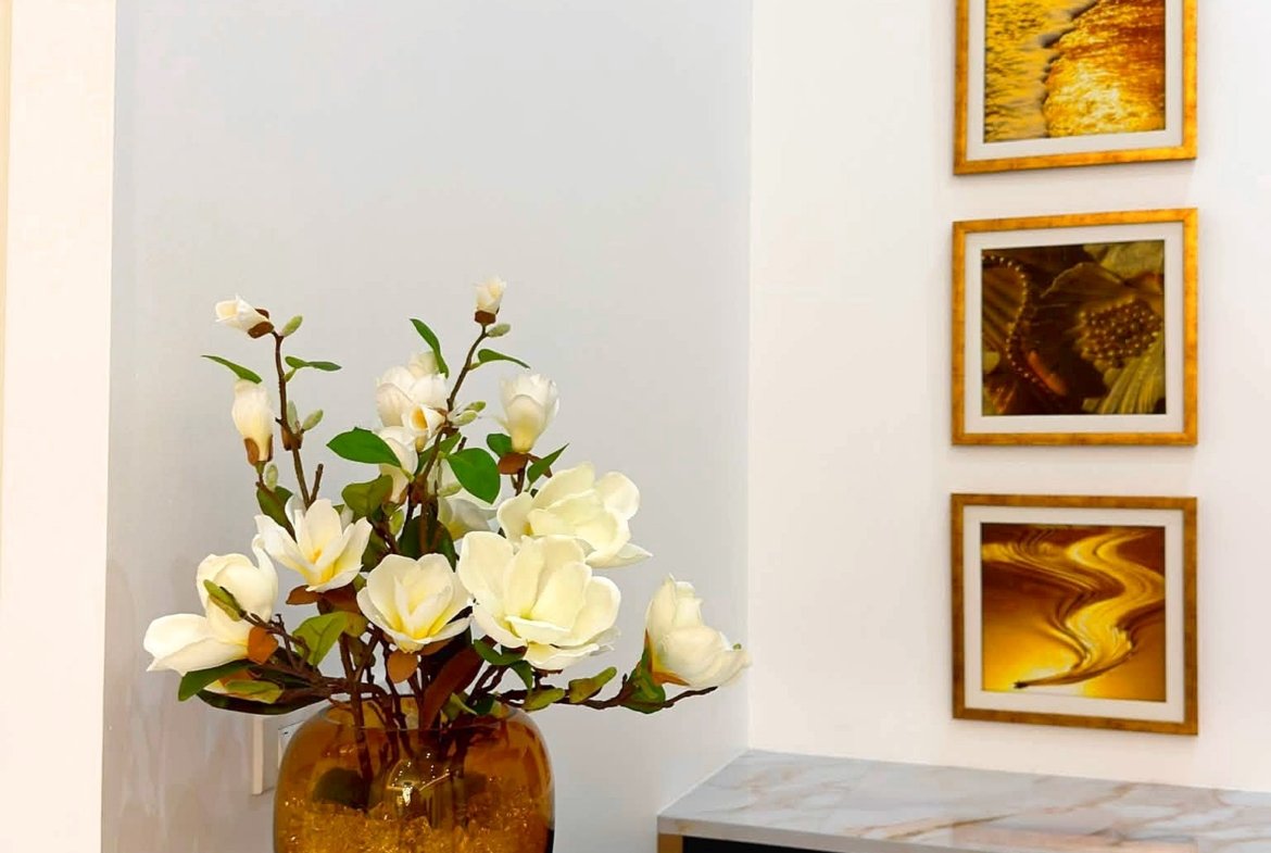 Amber glass vase with white magnolia flowers on a marble counter, with gold-framed wall art to the right.