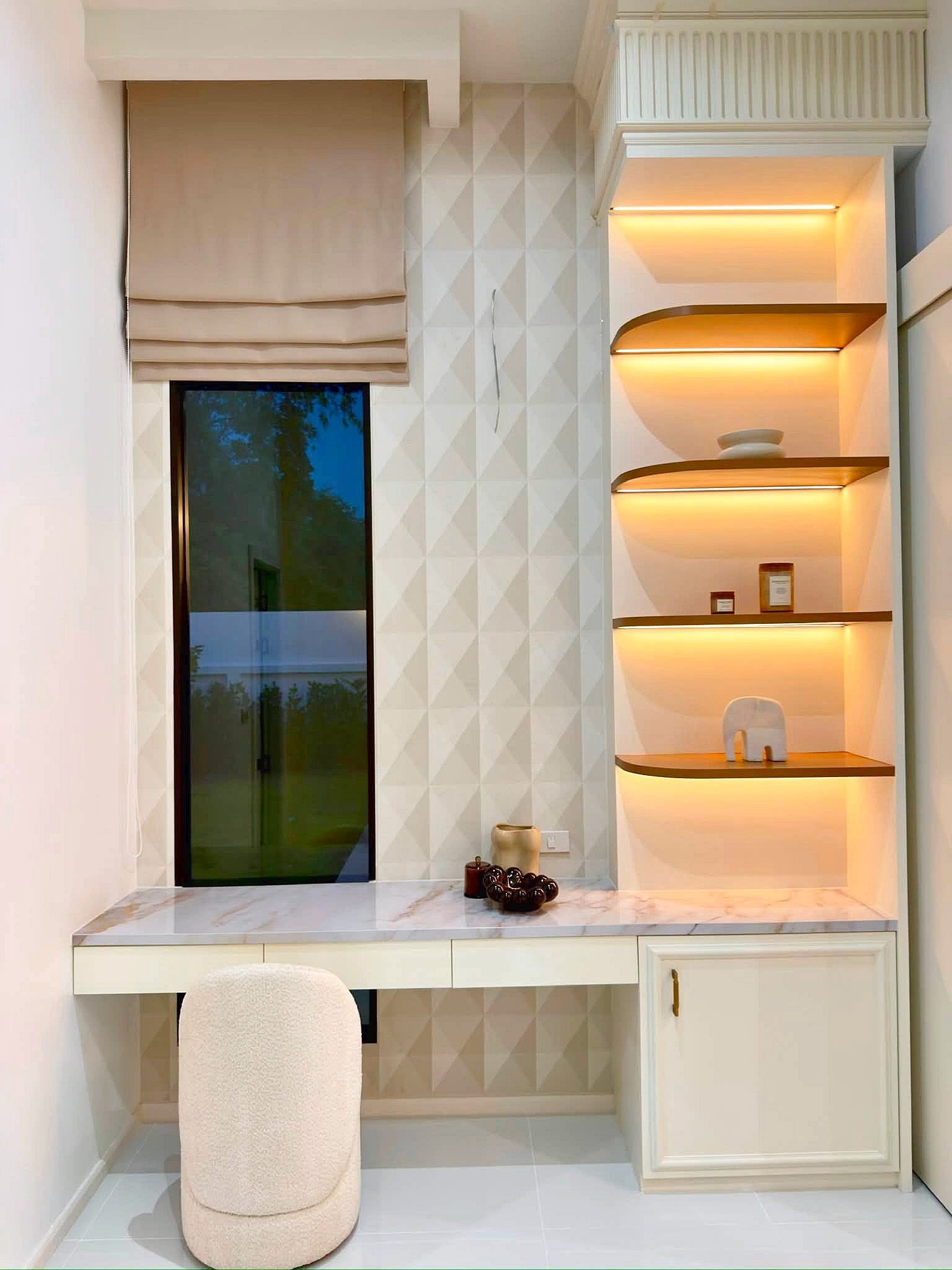 Poolvilla_Soi_Siam_Pattaya_Dlh584_9 Cream-toned bathroom vanity area with built-in illuminated shelves on the right, beige window shade to the left, and a marble-topped counter with a beige upholstered stool in front.