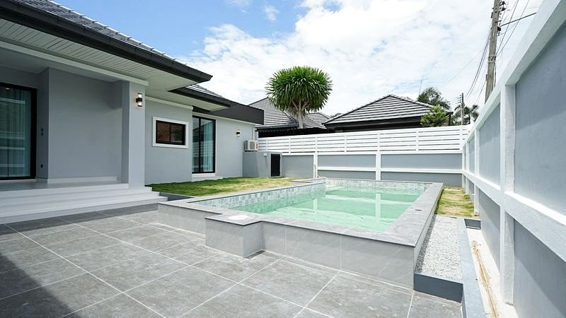 Modern house with a rectangular in-ground pool, gray tiled patio, and white privacy fence in a fenced backyard