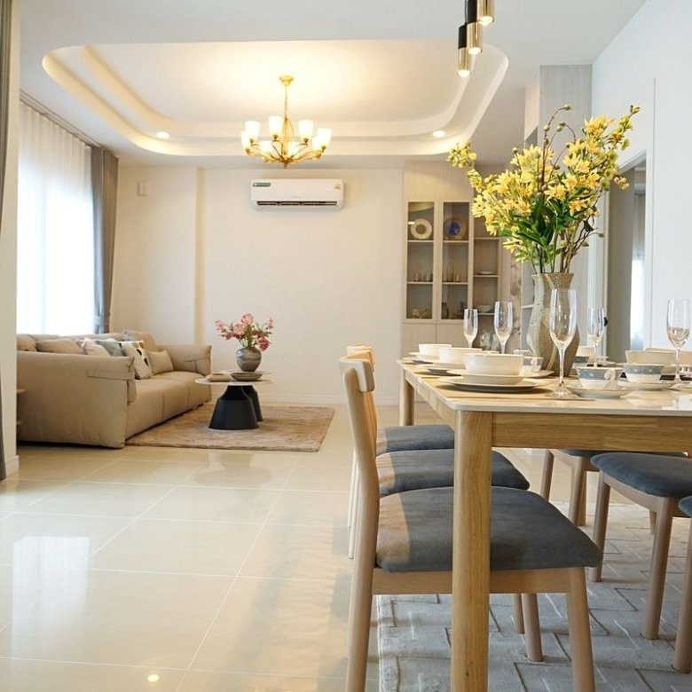 Bright open plan living and dining room with a wooden table set for six a vase of yellow flowers and a beige sofa in the background