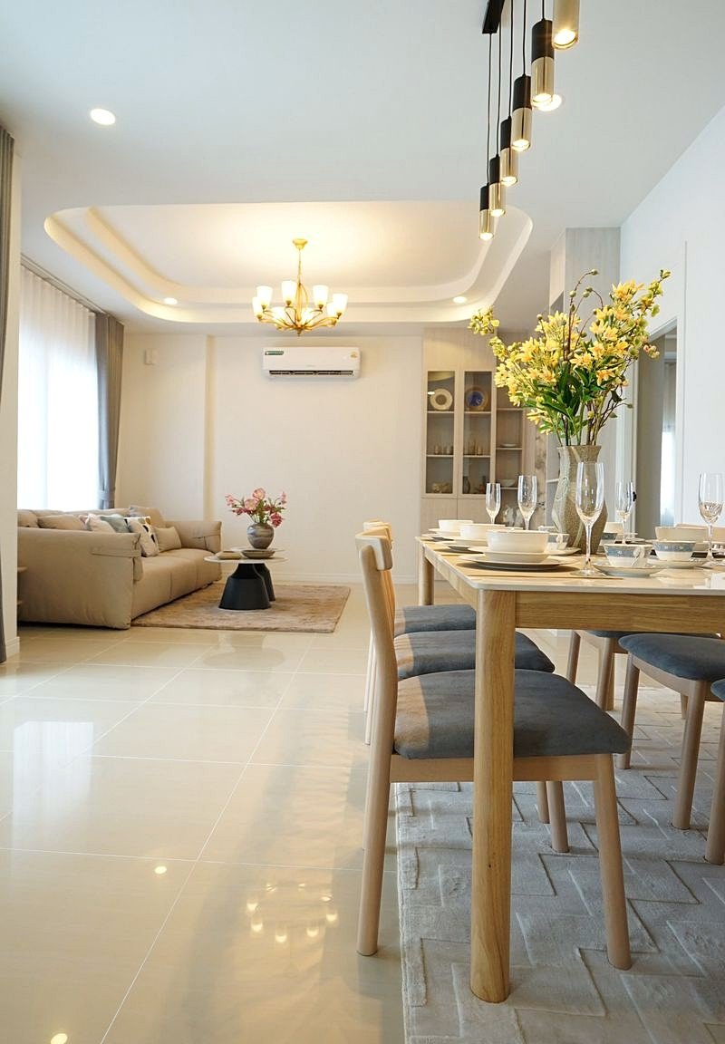 Pornthep_2_Village_Pattaya_Dlh578_10 Bright open-plan living and dining room with a wooden table set for six, a vase of yellow flowers, and a beige sofa in the background.