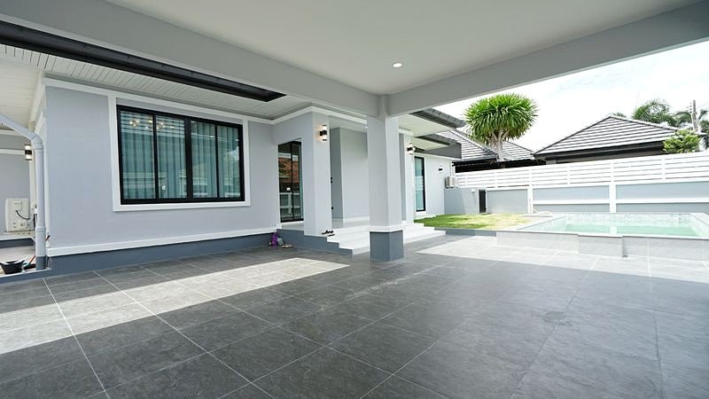 Modern single-story home with a covered gray-tiled patio, a large window, and a rectangular pool in a fenced backyard.