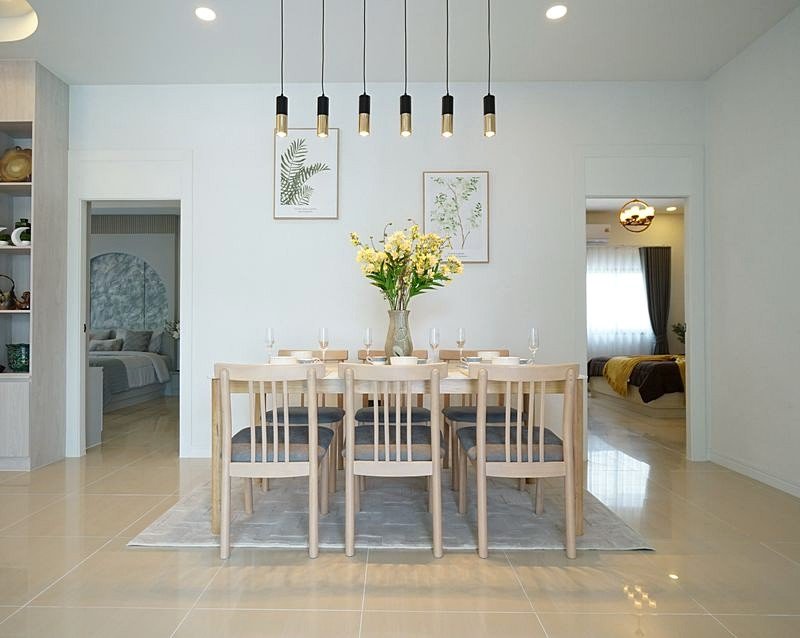 Light-filled dining room with a wooden table set for ten, a vase of yellow flowers, and black pendant lights above.