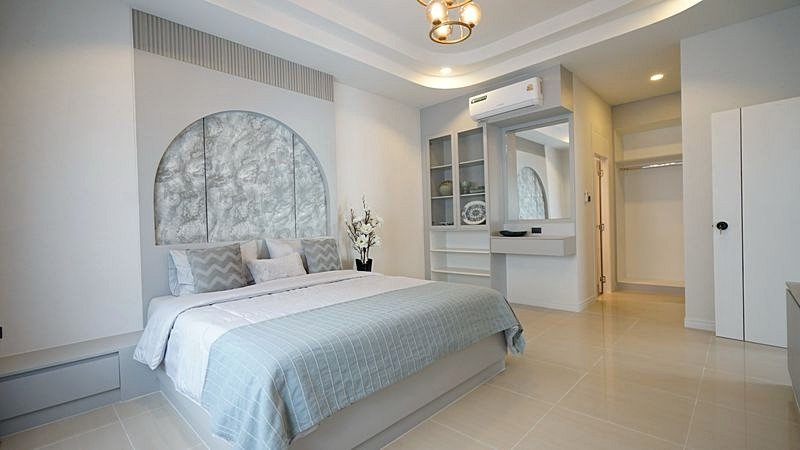 Bright modern bedroom with a low platform bed, pale blue bedding, and a circular paneled headboard; built-in shelves and a mirror nearby.