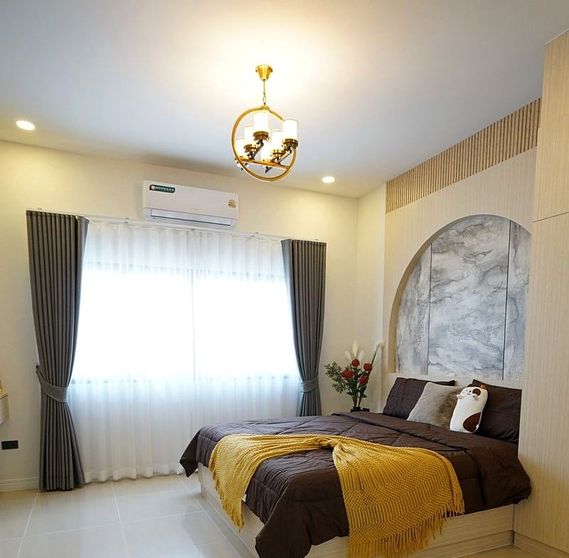 Bright bedroom with a large double bed, brown bedding, a mustard-yellow throw, marble arched headboard, and a gold chandelier.
