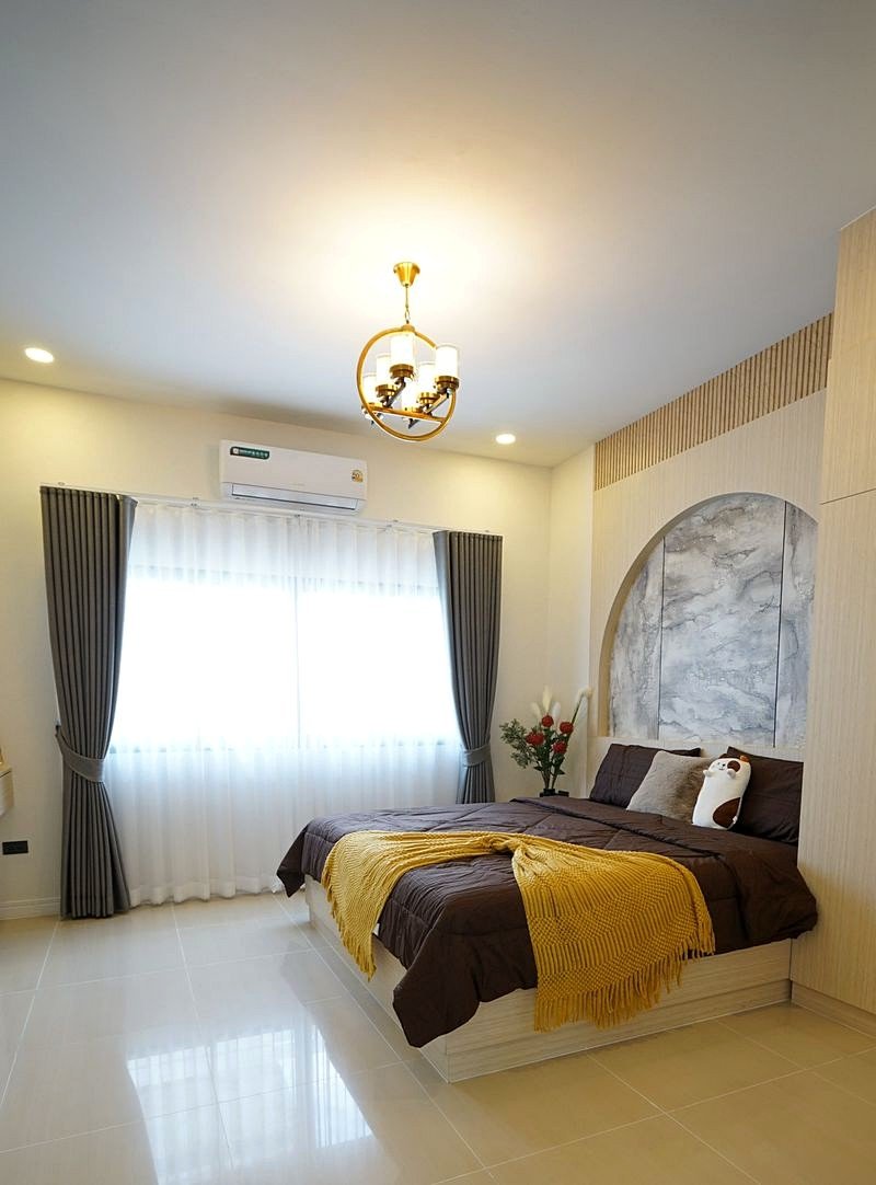 Pornthep_2_Village_Pattaya_Dlh578_9 Bright bedroom with a large double bed, brown bedding, a mustard-yellow throw, marble arched headboard, and a gold chandelier.