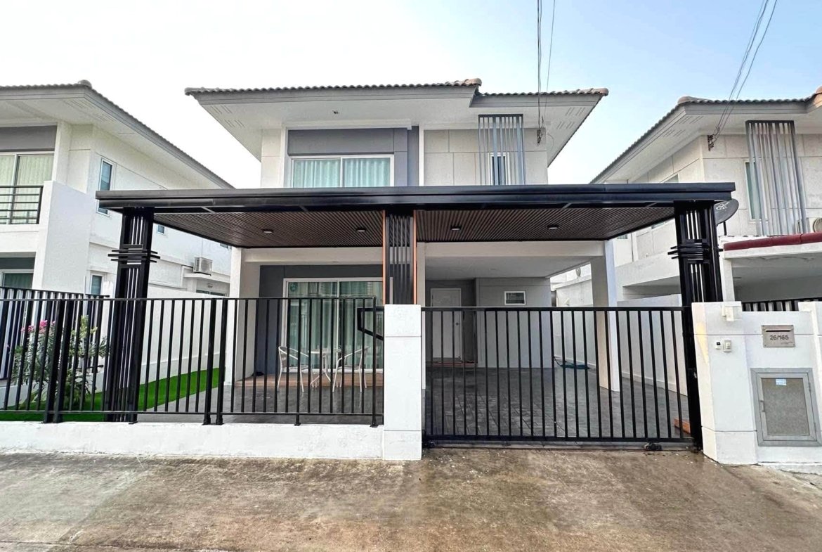 Front view of a modern row of white townhouses with a covered carport, black metal fence and gated entrance.