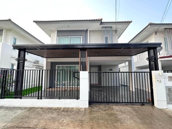 Front view of a modern row of white townhouses with a covered carport black metal fence and gated entrance