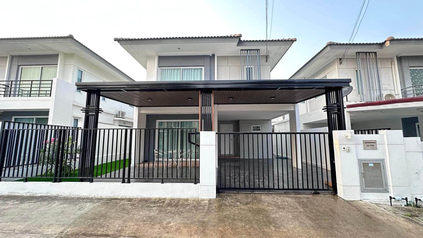 Pruksa_Nara_Pattaya_Rent_Rdl351 Front view of a modern row of white townhouses with a covered carport, black metal fence and gated entrance.