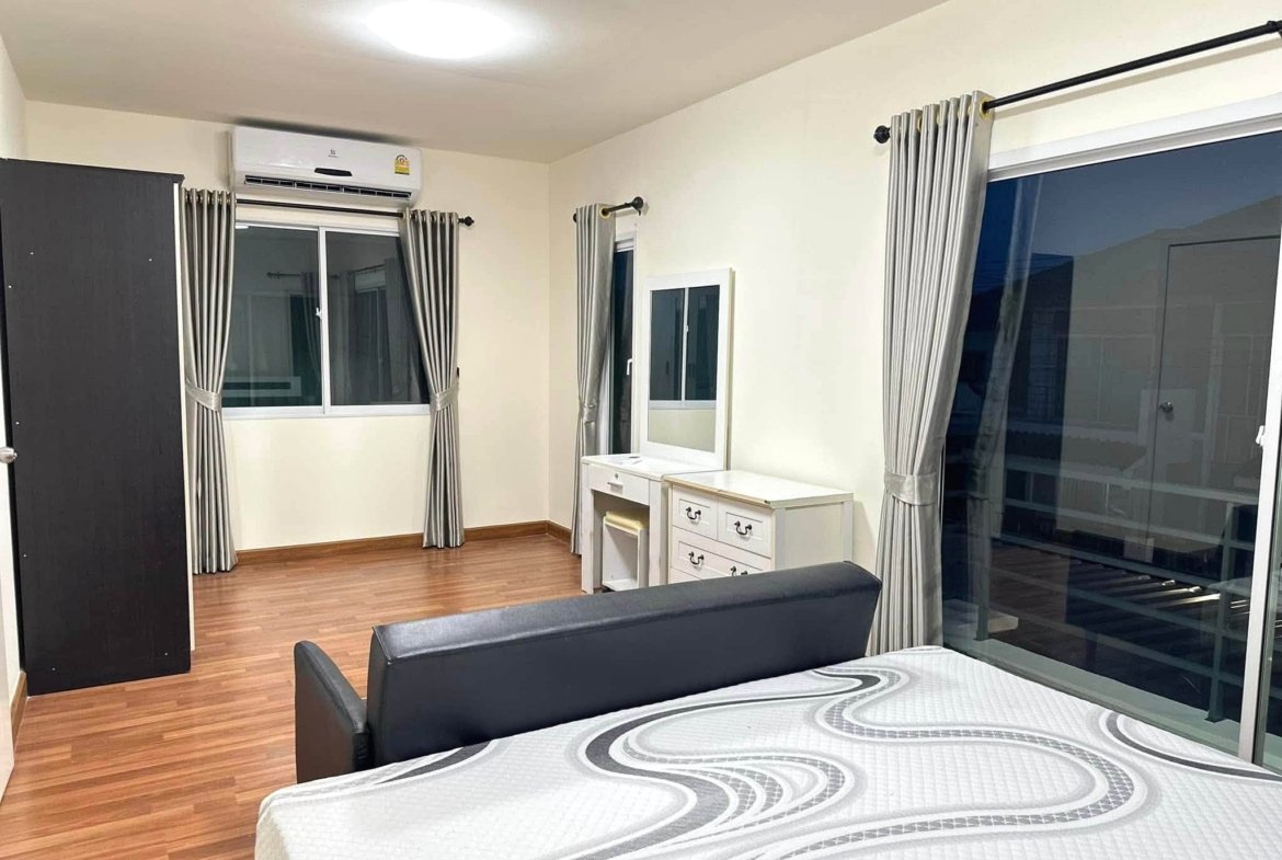 Hotel-style bedroom with two matching beds, dresser, mirror, and large windows with gray curtains.
