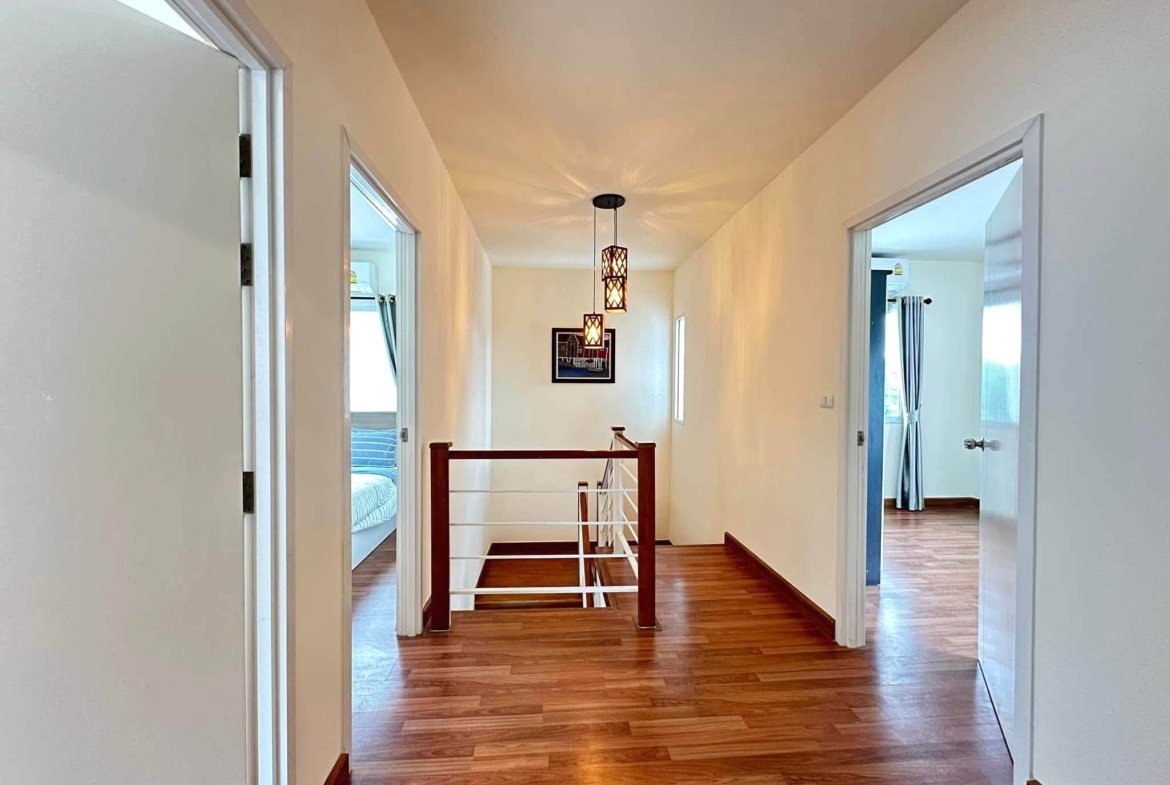 Bright home hallway with hardwood floor, open bedroom doors, and hanging lantern-style pendant lights along a white wall.