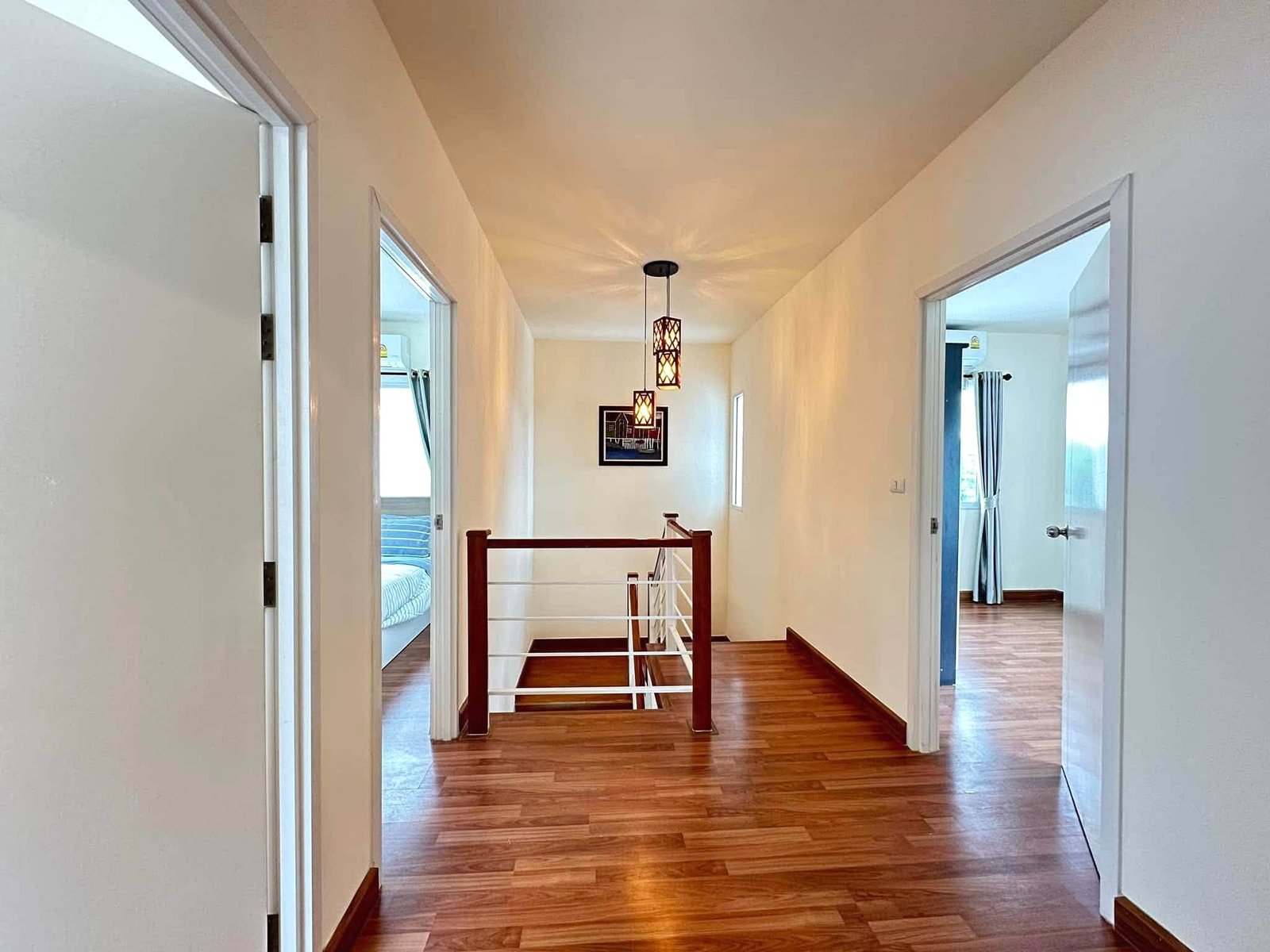Pruksa_Nara_Pattaya_Rent_Rdl351_13 Bright home hallway with hardwood floor, open bedroom doors, and hanging lantern-style pendant lights along a white wall.