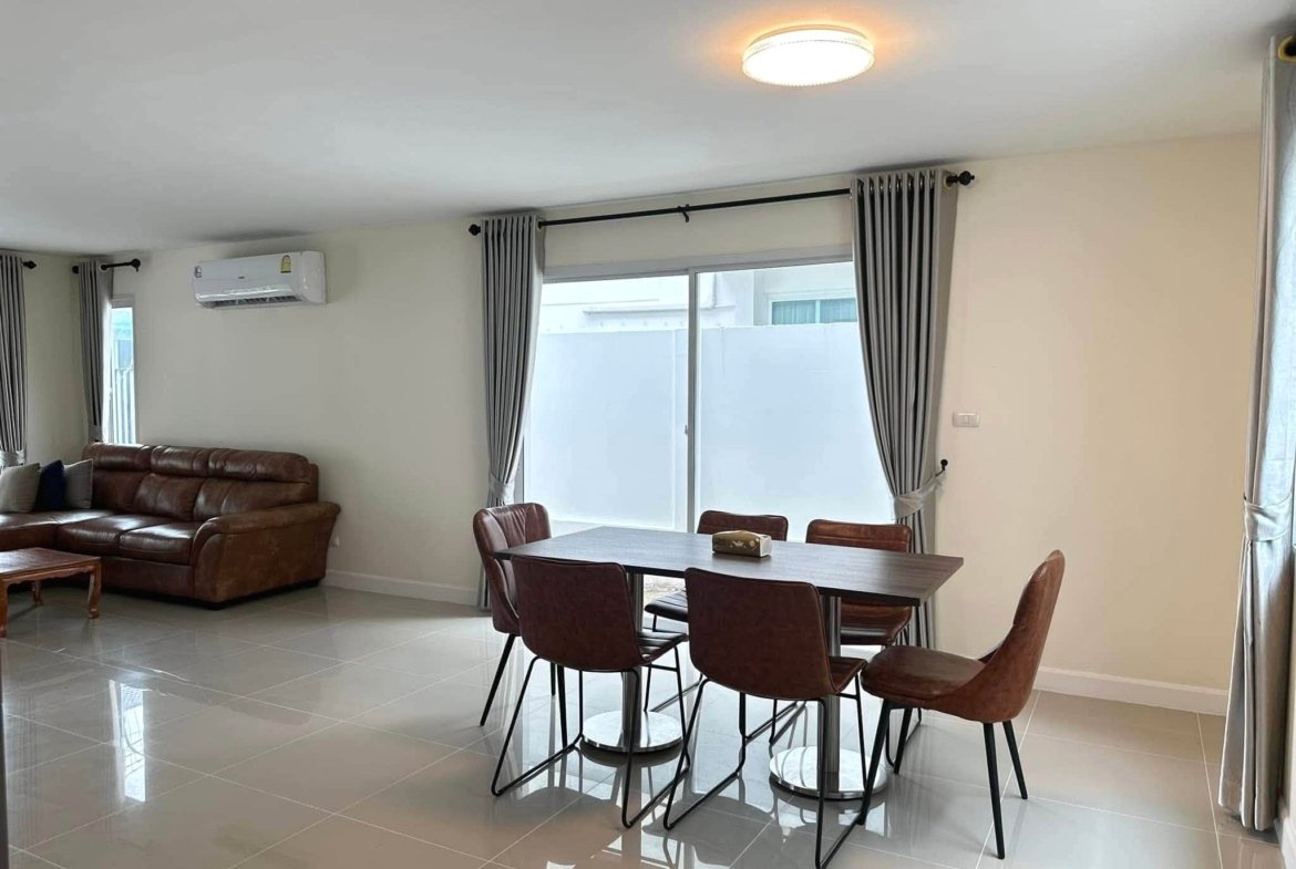 Open living and dining area featuring a brown leather sofa, a six-seat dining table with chairs, tiled floor, and large windows with gray curtains along the wall with an air conditioner above.