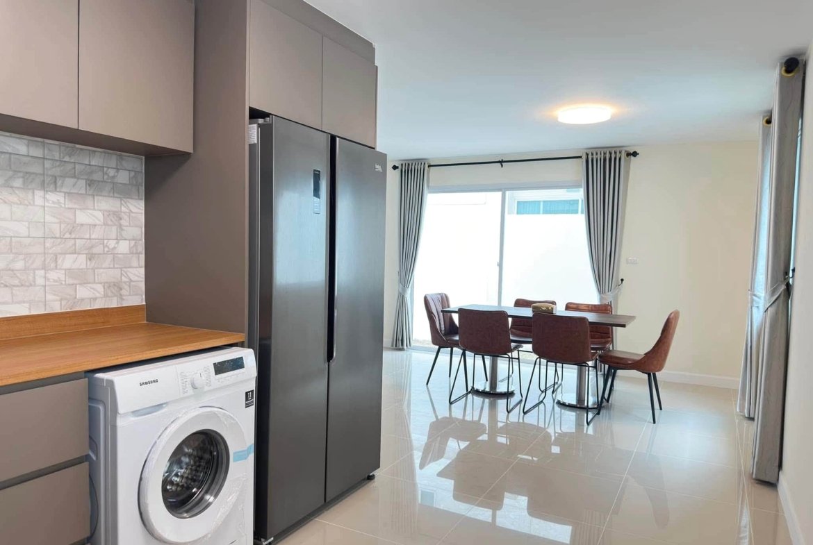 Modern kitchen with gray cabinets, stainless steel side-by-side fridge, and a front-loading washing machine under a wooden counter.