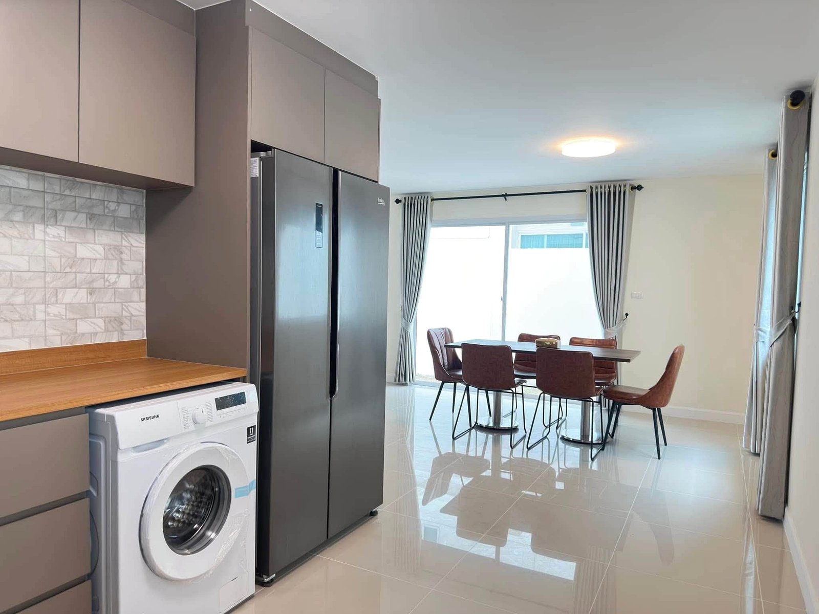Pruksa_Nara_Pattaya_Rent_Rdl351_4 Modern kitchen with gray cabinets, stainless steel side-by-side fridge, and a front-loading washing machine under a wooden counter.