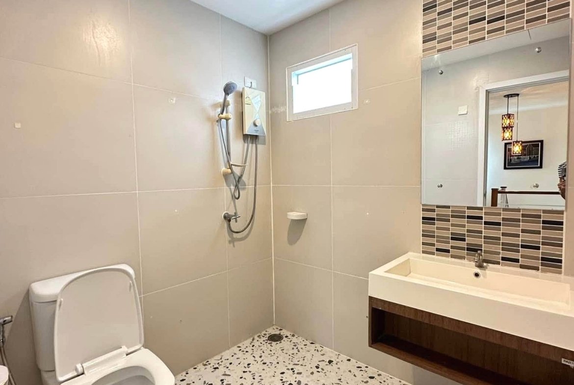 Modern bathroom with terrazzo floor, wall tiles, a walk-in shower, and a rectangular mirror above a white sink.