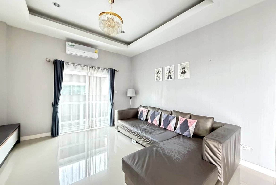 Living room with a gray sectional sofa, geometric throw pillows, and a glossy white floor surface.