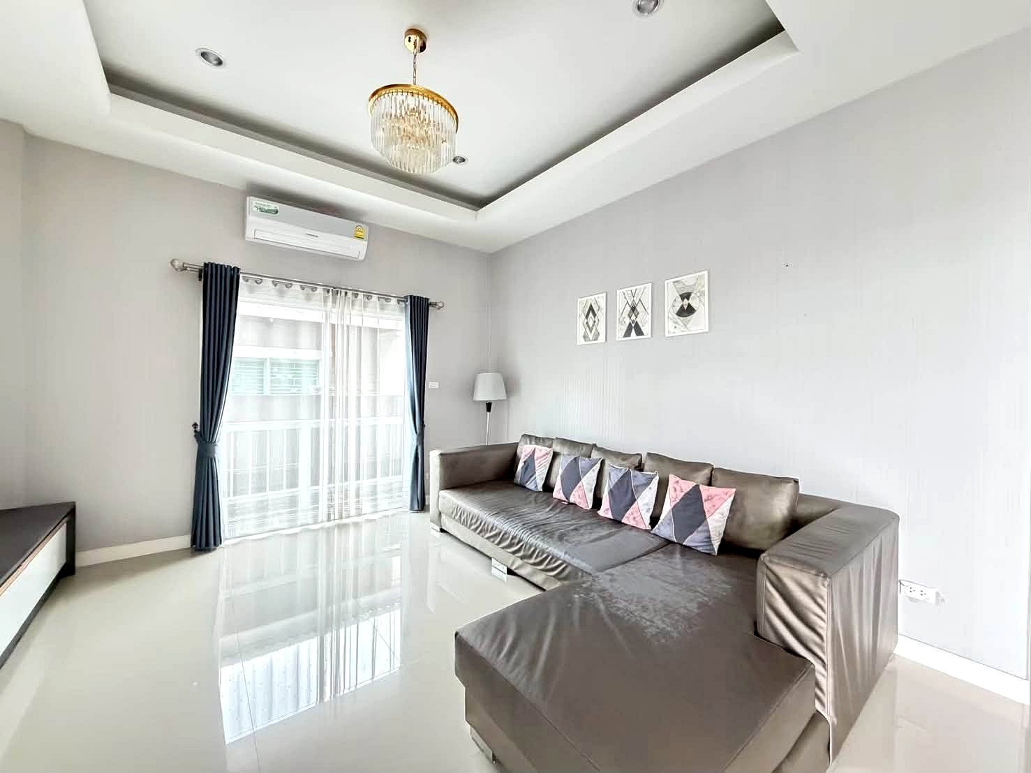 Raviporn_Romsai_Village_Dlh580_10 Living room with a gray sectional sofa, geometric throw pillows, and a glossy white floor surface.