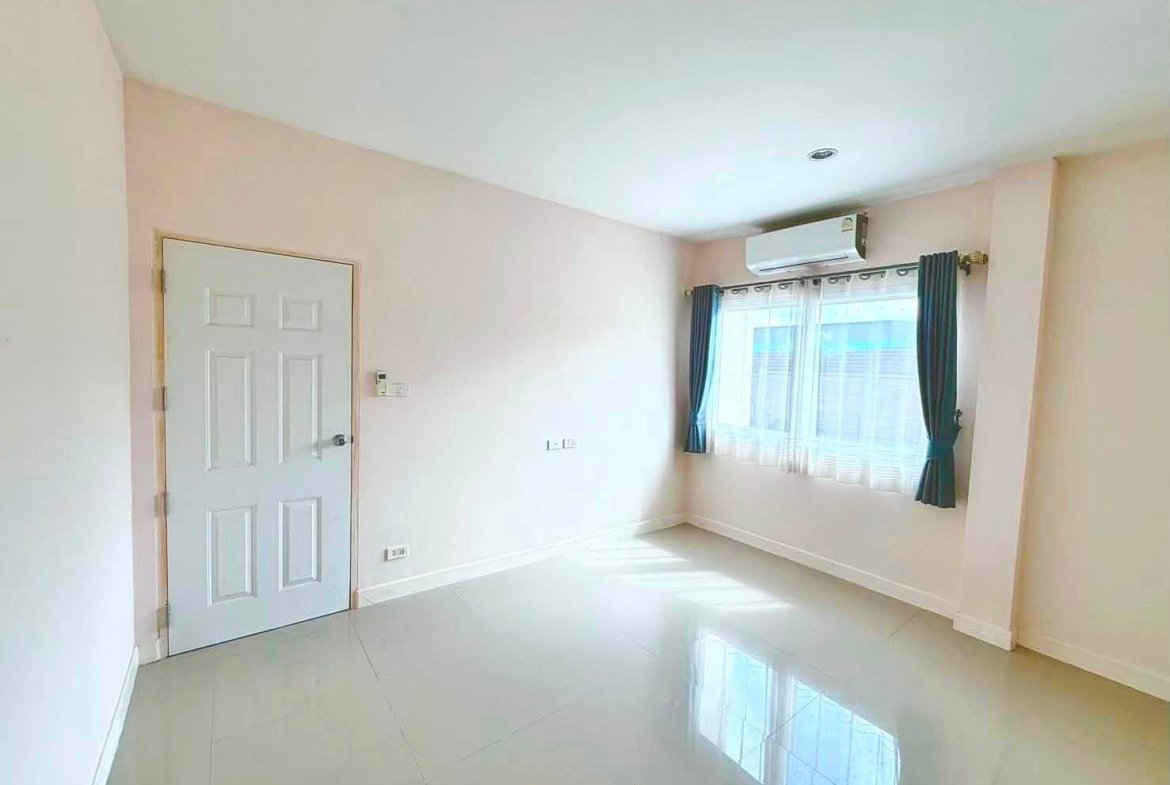 Empty bright room with pale pink walls, white door, large window with blue curtains, and a wall-mounted air conditioner above the window.