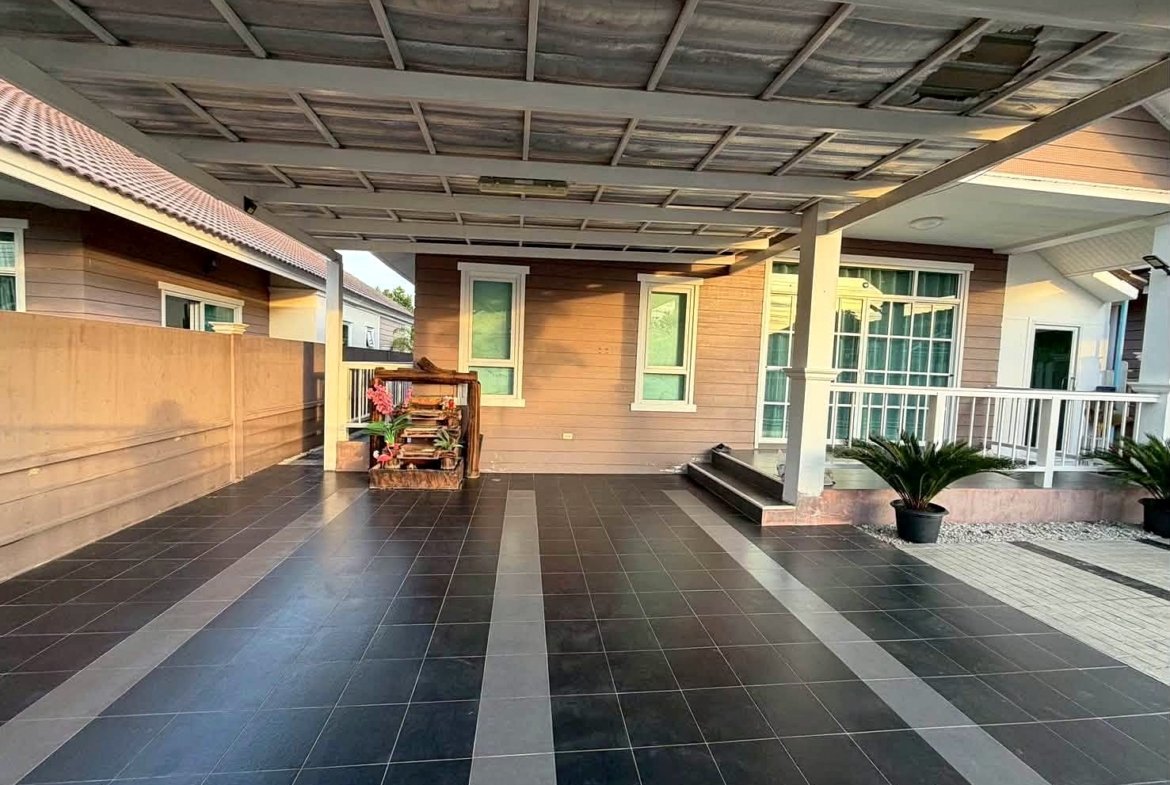 Covered porch of a modern home with dark tile flooring, beige walls, white-framed windows, railing, and potted plants.