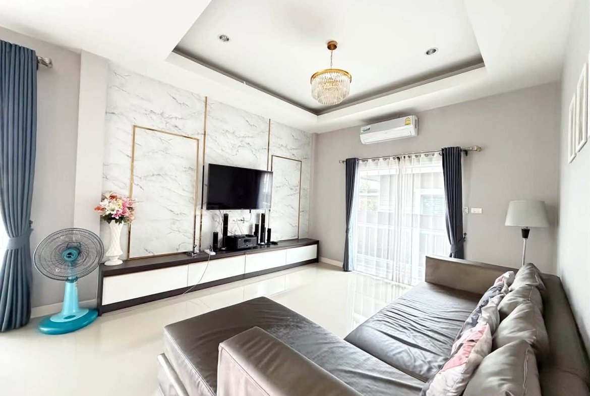 Bright modern living room with a gray sectional sofa, marble-panel TV wall, and a wall-mounted TV above a white storage console.