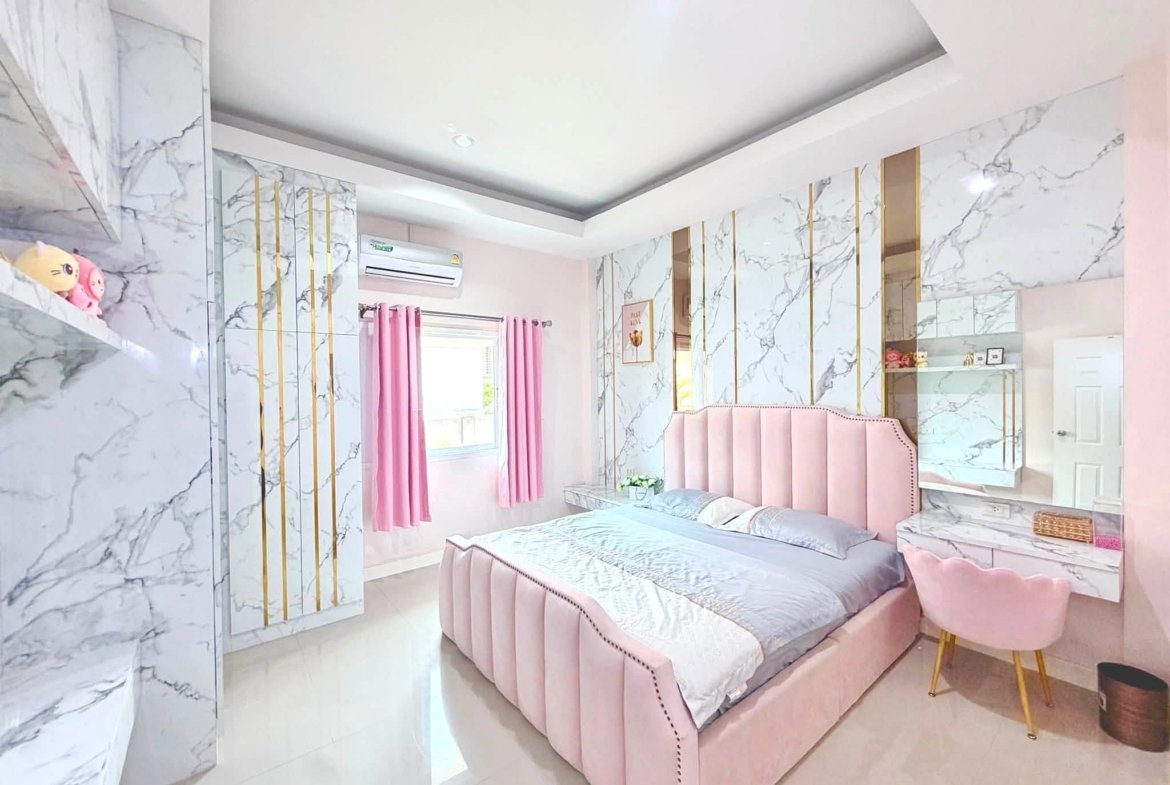 Pastel pink bedroom with marble-pattern walls, twin beds with pink headboards and matching pink curtains.
