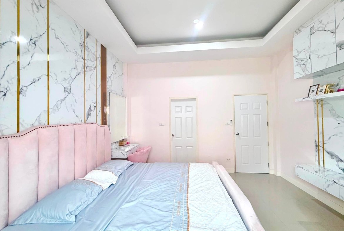 Pink upholstered bed against marble walls with gold vertical strips and white doors in a bright modern bedroom.