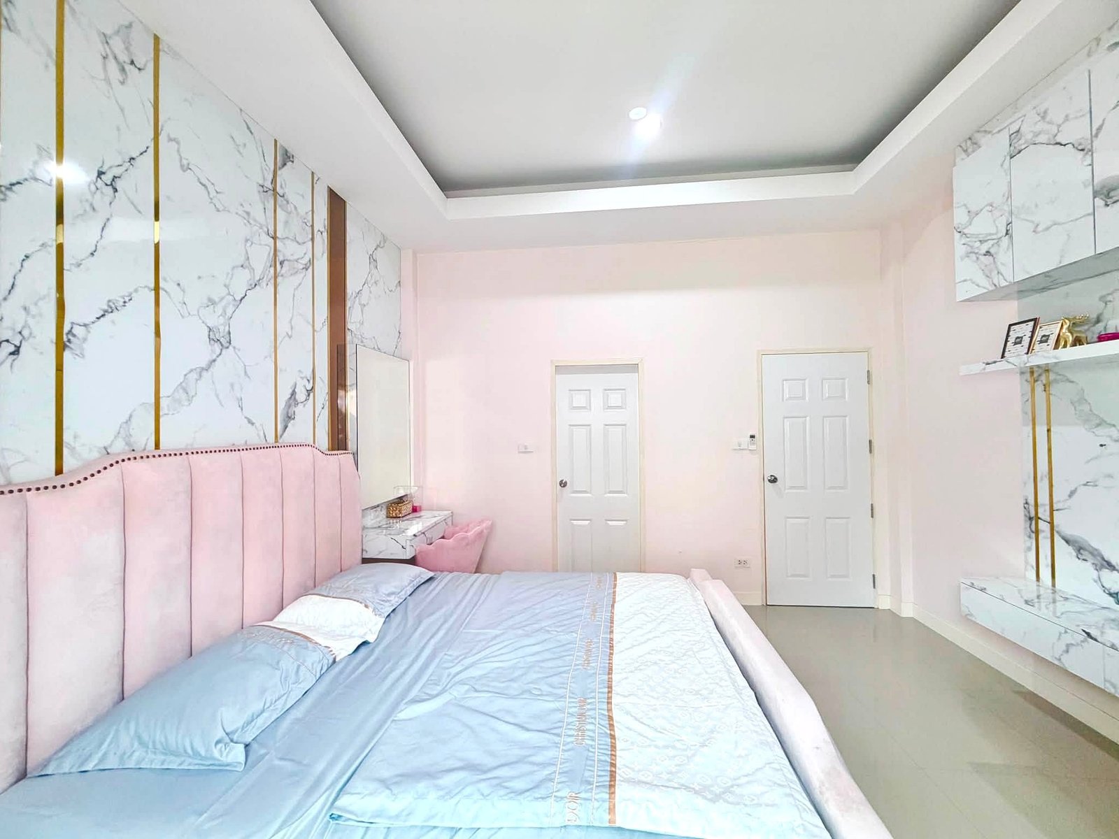 Raviporn_Romsai_Village_Dlh580_7 Pink upholstered bed against marble walls with gold vertical strips and white doors in a bright modern bedroom.