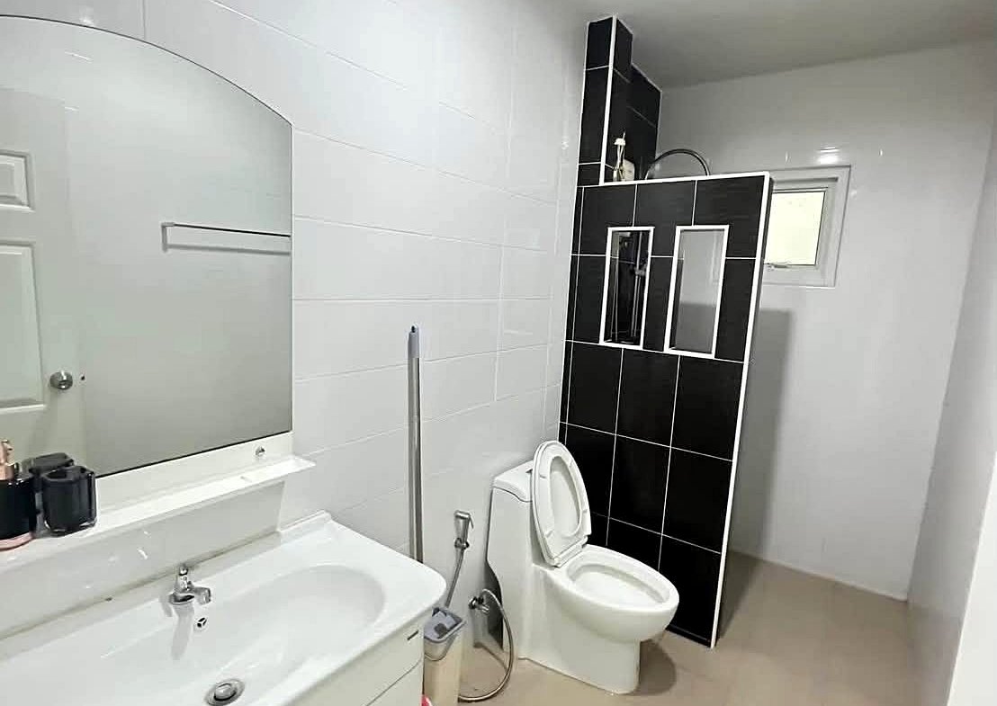 Modern bathroom with white vanity, oval mirror, and toilet; black tiled shower divider in the corner.