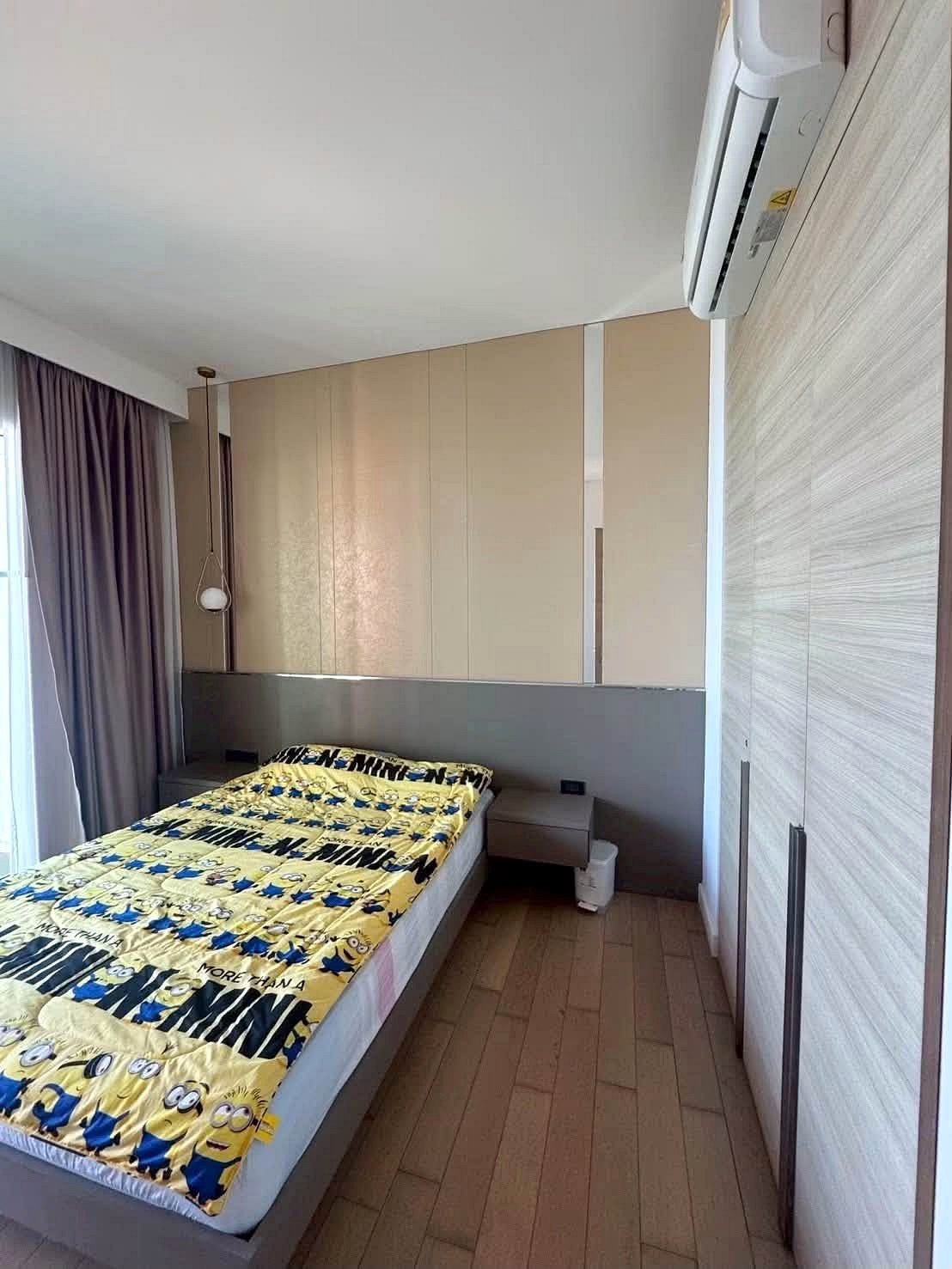 Reflectiom_Jomtien_2Bed_Dlc625_13 Small modern bedroom with a single bed, gray headboard, and yellow Minions blanket, set against built-in beige wardrobes and a pendant light above. Magnified windows with purple curtains on the left.